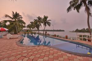 a swimming pool with palm trees and a body of water at Kalathil Lake Resort in Vaikom