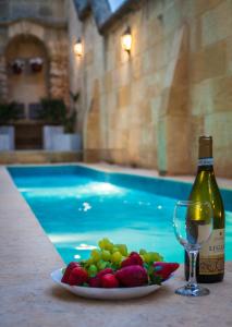 - une assiette de fruits et une bouteille de vin à côté de la piscine dans l'établissement Id Dar Ta Censu, à Qala
