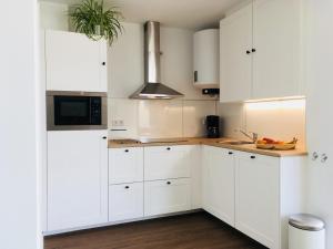 a white kitchen with white cabinets and a microwave at Appartement aan het strand, hond welkom in Zoutelande