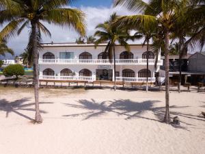 un edificio sulla spiaggia con palme in primo piano di Hotel Albemarle a Puerto Villamil