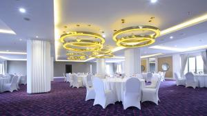 a banquet hall with white tables and chairs and chandeliers at Shakti Hotel Bandung in Bandung