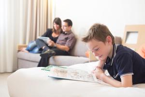 Un jeune garçon qui se couche sur une table en lisant un livre dans l'établissement Novotel Breda, à Breda