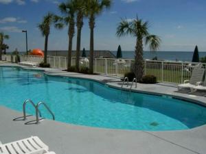 a large swimming pool with palm trees and the ocean at JeffsCondos - 1 Bedroom - Camelot Resort in Myrtle Beach