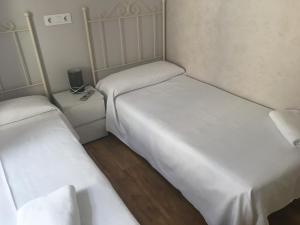 two beds in a small room with white sheets at Albergue Santiago Apostol in Logroño