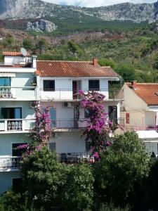 a white apartment building with purple flowers on the balconies at Apartmani Ivona s pogledom na more in Podgora