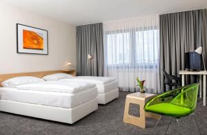 a hotel room with two beds and a green chair at Tryp by Wyndham Frankfurt in Frankfurt