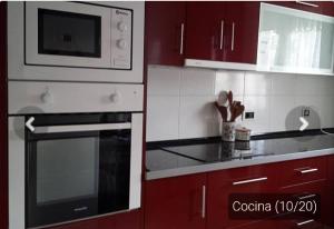 a kitchen with red cabinets and a stove and microwave at Casa _pareada con piscina y jardin privado in Torredembarra