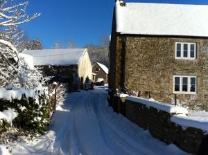 eine schneebedeckte Straße neben einem Steingebäude in der Unterkunft Bake House Cottage in Shepton Mallet