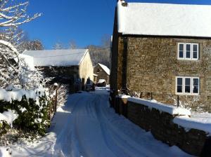 a snow covered road next to a stone building at Bake House Cottage in Shepton Mallet