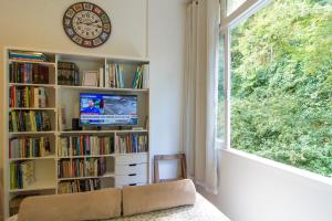 a room with a book shelf with a clock and a window at Flat 407 in Petrópolis
