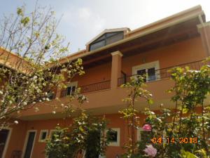 an orange building with a balcony and some trees at Pitsinis Apartments in Roda