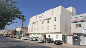 a white building with cars parked in a parking lot at Towlan Al Rawdah تولان للشقق المخدومة فرع الروضة in Riyadh