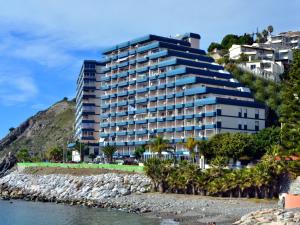 a building on a hill next to a body of water at Arrayanes Playa Almuñecar in Almuñécar
