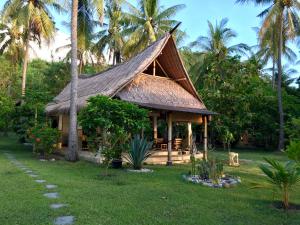 una casa con tetto di paglia e palme di The Papalagi Resort a Gili Gede