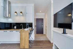 グダニスクにあるElite Apartments Kwartal Kamienicの白いキャビネットと薄型テレビ付きのキッチンが備わります。
