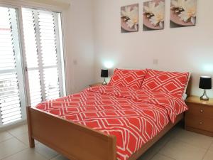 a bedroom with a bed with a red comforter and two windows at Limnaria Westpark in Paphos