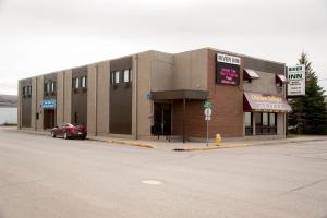 a building on a street with a car parked in front at River Inn in Nipawin