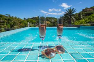 two glasses and sunglasses on a table next to a swimming pool at Pousada Renda do Mar in Morro de São Paulo