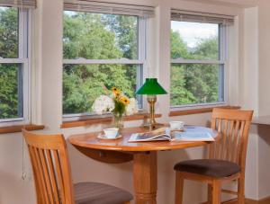 a table with chairs and a lamp and two windows at West Hill House B&B in Mad River Valley in Warren