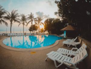 a swimming pool with white lounge chairs and palm trees at Coral Resort & Bungalows in Haad Rin