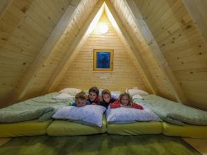 three children laying on pillows on a bed in a tree house at Camp Podljubelj in Podljubelj