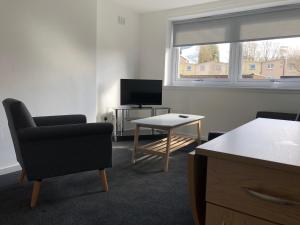 a living room with a chair and a tv and a table at Glenrothes Central Apartments - One bedroom Apartment in Glenrothes