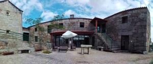 un edificio de piedra con una mesa y una sombrilla en Guesthouse Casa das Abegoarias en Celorico de Basto