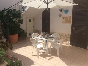 une table blanche avec des chaises blanches et un parasol dans l'établissement Appartamenti Monacò, à San Vito Lo Capo