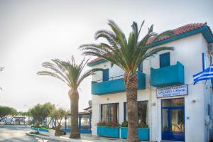 a hotel with palm trees in front of a building at Galazio Limani - Rooms to let in Moúdhros