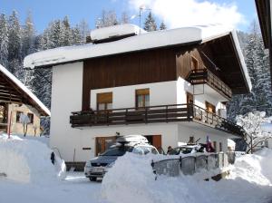 a house covered in snow with cars parked in front at Casa De Biasio PM in Falcade