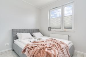 a white bedroom with a large bed with a blanket on it at Elite Apartments Oliwa Business Center in Gdańsk
