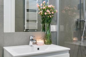 a vase of pink flowers sitting on a bathroom sink at Elite Apartments Oliwa Business Center in Gdańsk
