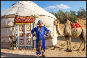 a man standing next to a camel in front of a yurt at Aidar Yurt Camp in Taldy