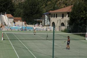 twee kinderen die tennissen op een tennisbaan bij Camping Les Prades in Mostuéjouls