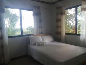 een slaapkamer met een bed met 2 ramen en witte lakens bij Villa Feliza in Loboc