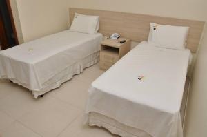 two beds with white sheets in a room at Beija - Flor Hotel in Ipiaú