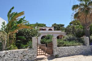 a house with a stone wall and palm trees at Villa Hibisco in San Vito lo Capo