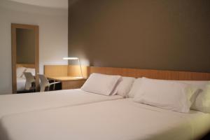 uma grande cama branca num quarto com uma secretária em Hostal Abodi em Pamplona