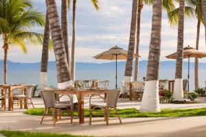 a table and chairs on the beach with palm trees at Vista Vallarta All Suites On The Beach in Bucerías