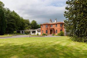 a large brick house with a green lawn in front of it at Woodland House Hotel in Dumfries