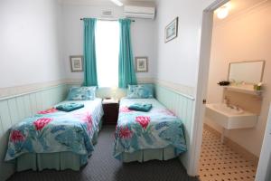 two beds in a room with a sink and a mirror at Jacaranda Guest House in Busselton
