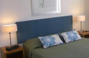 a bedroom with a bed with a blue headboard and two lamps at Meridian Caloundra in Caloundra