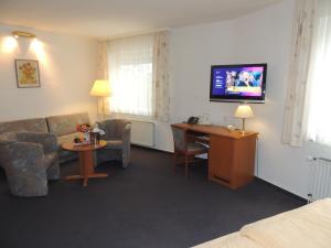 a living room with a couch and a desk and a tv at Hotel-Restaurant zum Roeddenberg in Osterode