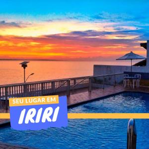 a resort swimming pool with a sunset in the background at Hotel Portal da Lua in Iriri