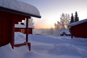 a snow covered cabin with the sun setting in the background at Peurasuvanto Mökit & Camping in Peurasuvanto