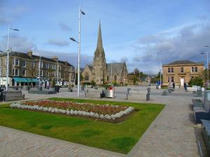 a town square with a park with flowers and a church at Snug - Tùr Sealladh Apartment in Helensburgh