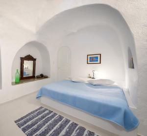 a white bedroom with a blue bed and a mirror at Chelidonia Traditional Villas in Oia