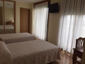 1 dormitorio con 2 camas, mesa y ventana en Hostal Santa Baia, en Ribadumia