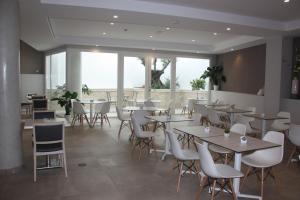 a restaurant with tables and white chairs and windows at Hotel Puerta del Mar - Adults Recommended in Nerja