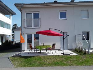 une table et des chaises avec un parasol rouge devant une maison dans l'établissement Haus am Leuchtfeuer, à Peenemünde